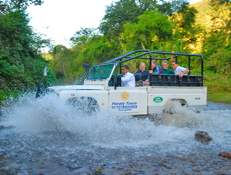 Offener 4x4-Jeep mit Fahrgästen fährt durch einen Fluss