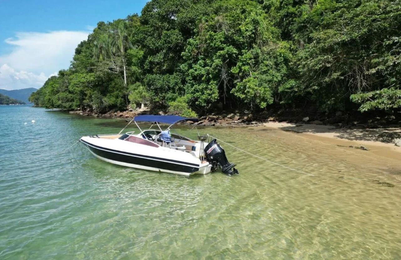 Lancha anclada en el agua poco profunda y transparente de una playa rodeada de selva