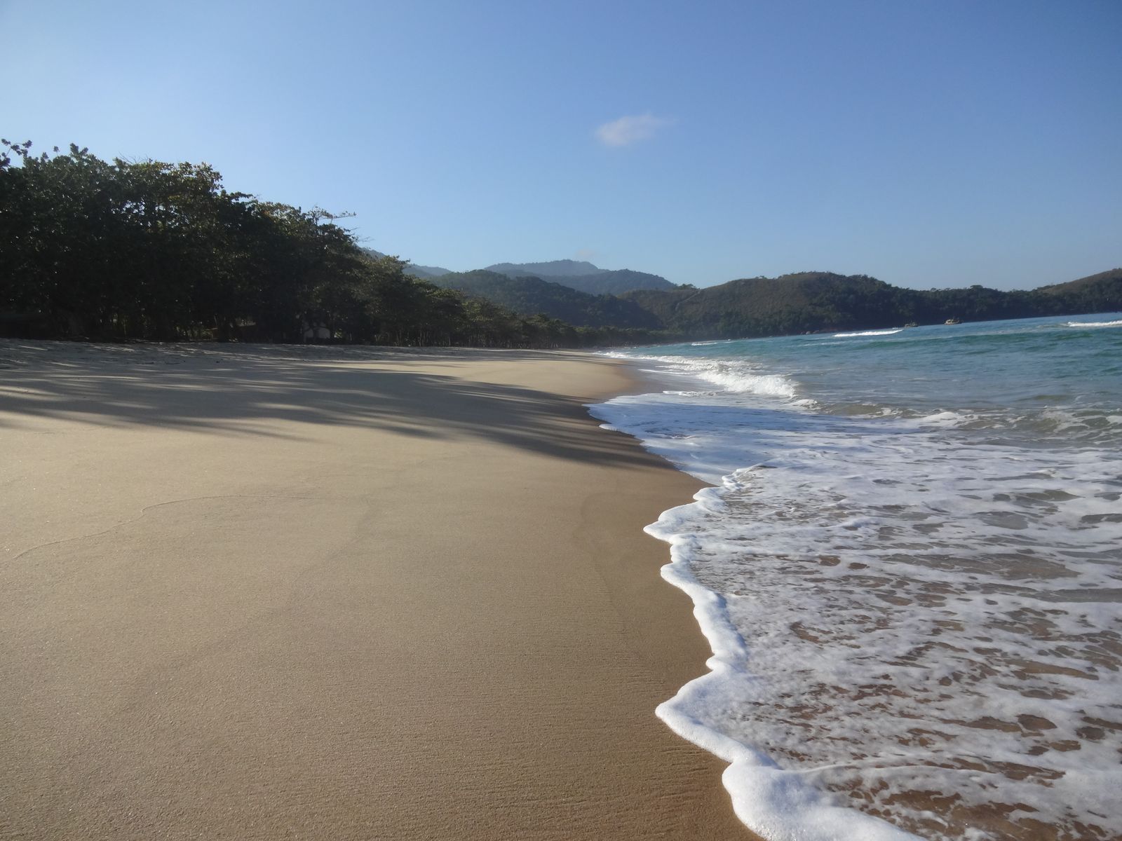Larga playa de arena dorada con olas y cerros cubiertos de selva