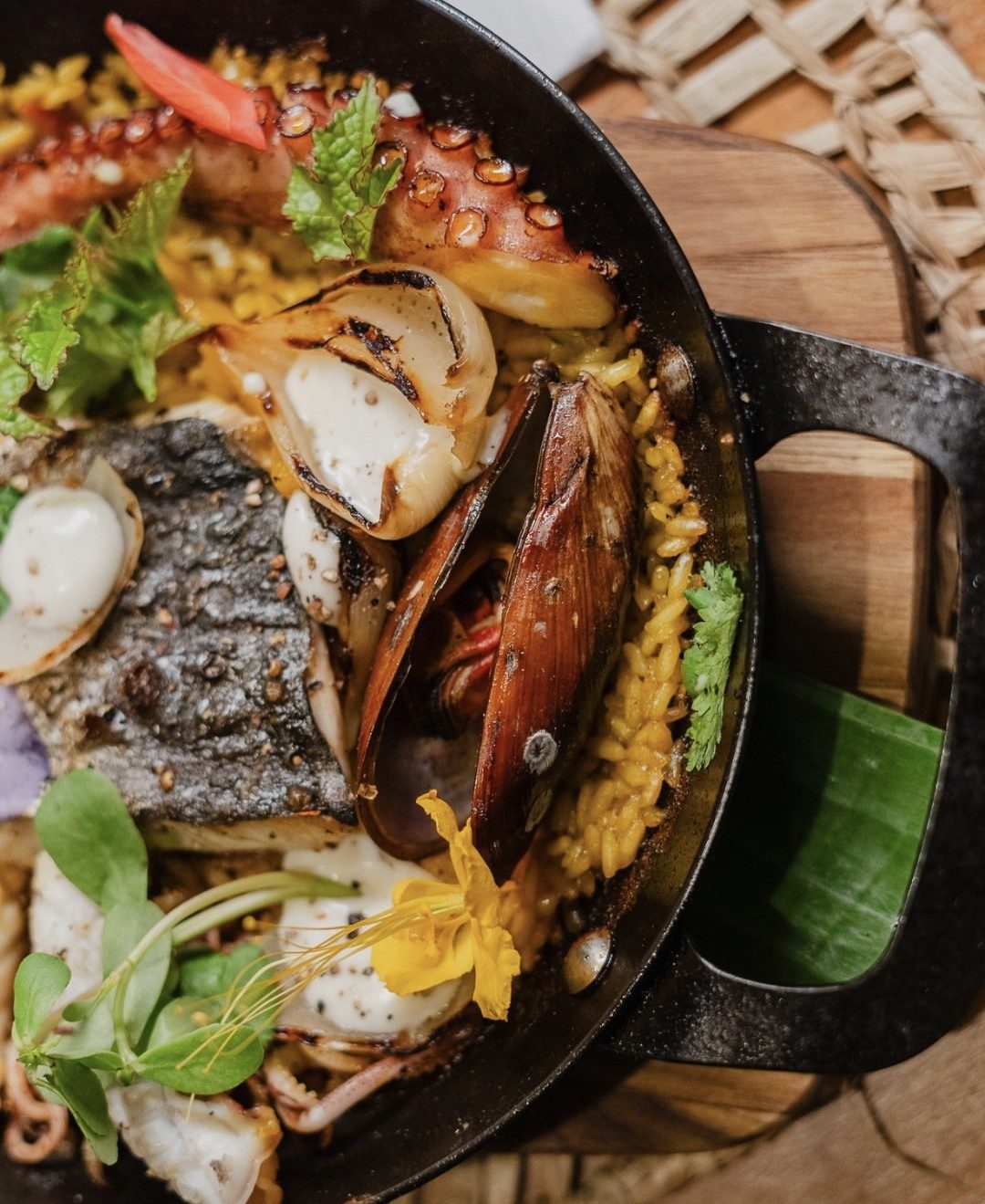 Paella de fruits de mer dans une poêle en fonte vue de dessus : tentacule de poulpe, moule, calamar, oignon rôti et riz jaune