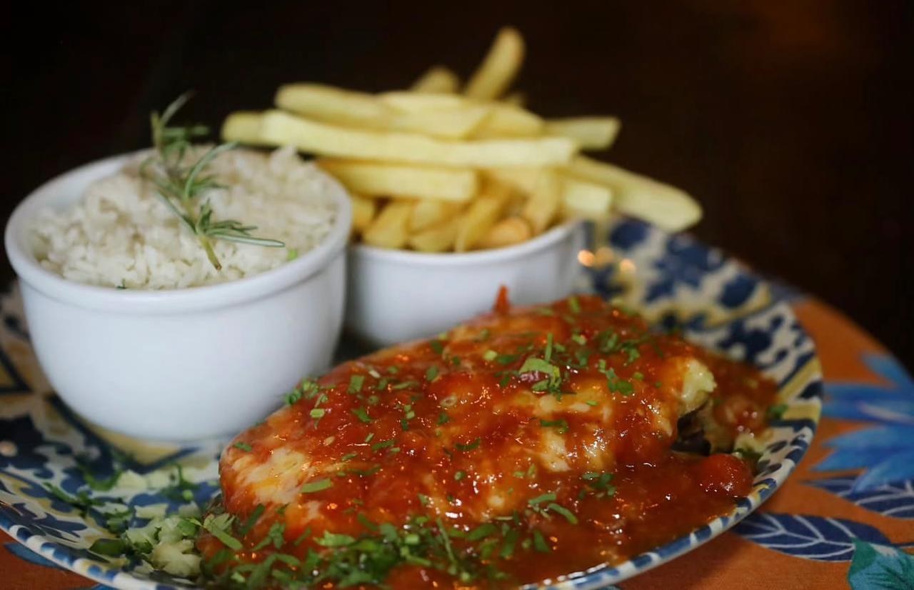 Parmegiana de filete mignon en un plato estampado: milanesa con salsa de tomate y queso gratinado, con arroz y patatas fritas al lado
