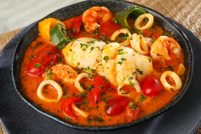 Moqueca de frutos do mar numa panela escura, com camarão, lula e pimentões