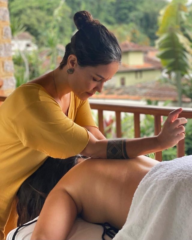 Terapeuta fazendo massagem numa hóspede, com a mata e os telhados de Paraty ao fundo
